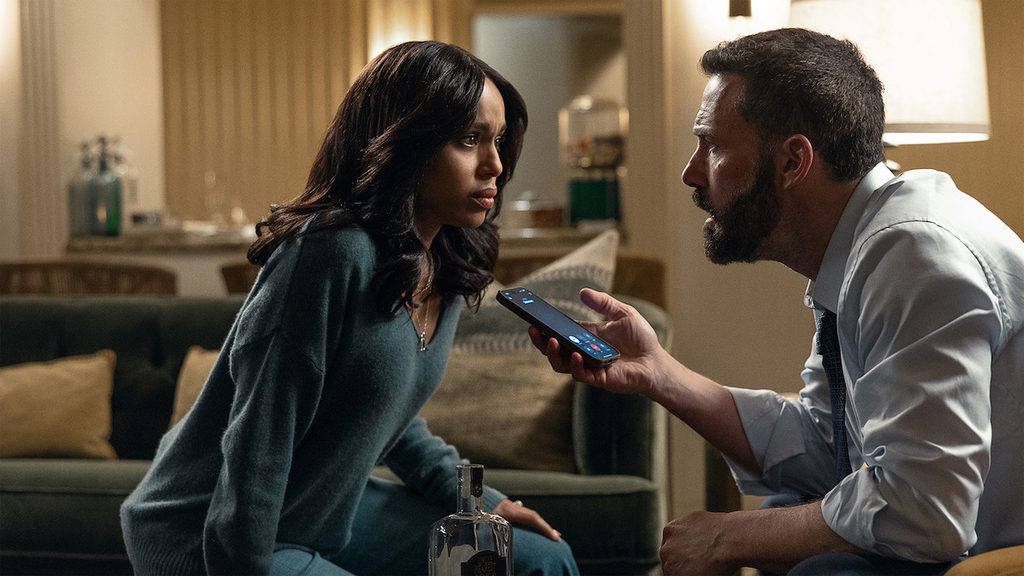 Ben Affleck sentado frente a una mujer mientras le muestra un teléfono móvil.