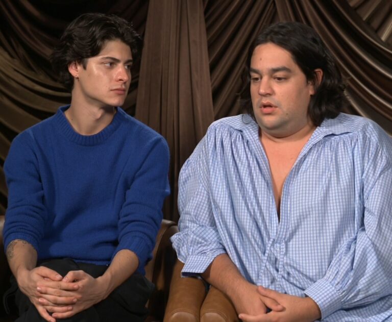 Milo Quifes y Carlos González sentados juntos durante una entrevista promocional con cortinas oscuras