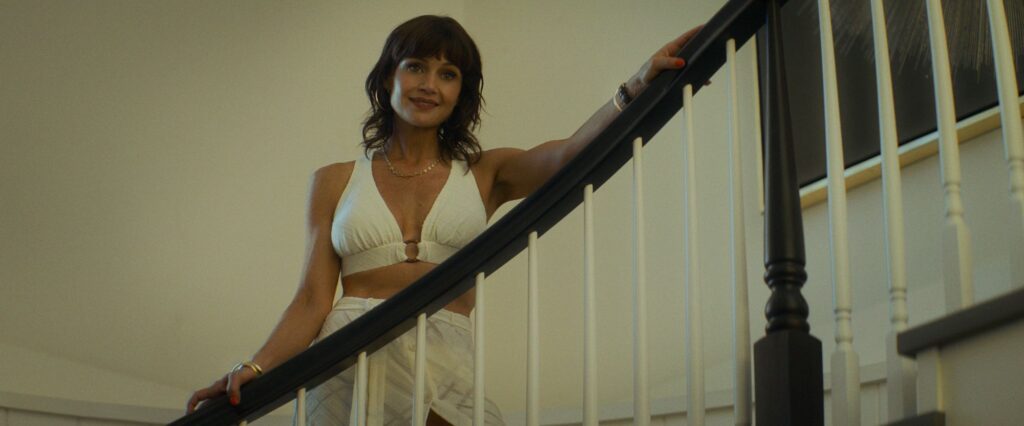 Carla Gugino apoyada en una barandilla de una escalera interior
