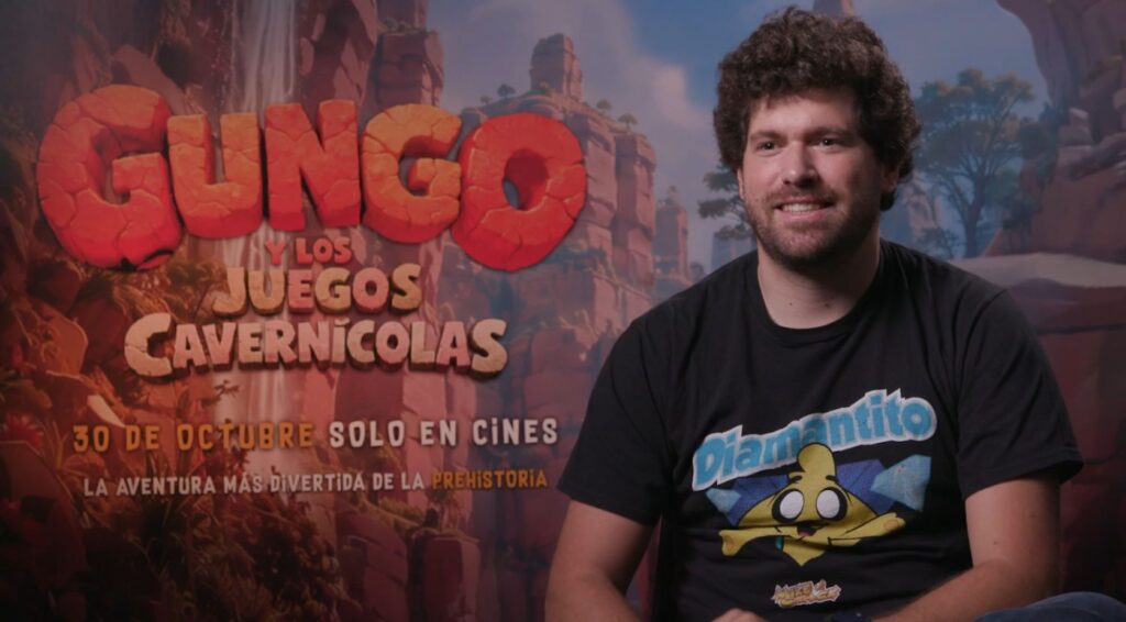 Mikecrack, con camiseta negra, sonríe durante una entrevista delante del cartel de Gungo y los juegos cavernícolas