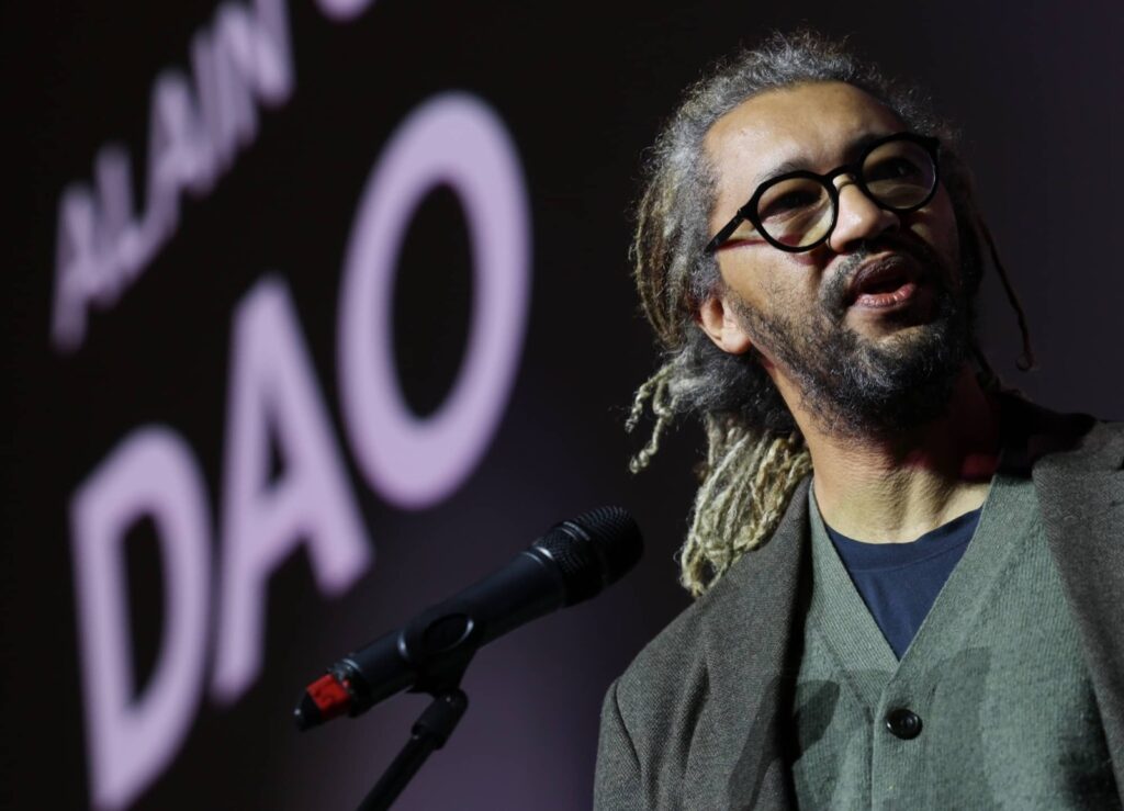 Alain Gomis habla ante un micrófono con el título Dao proyectado detrás, en la Seminci de Valladolid.