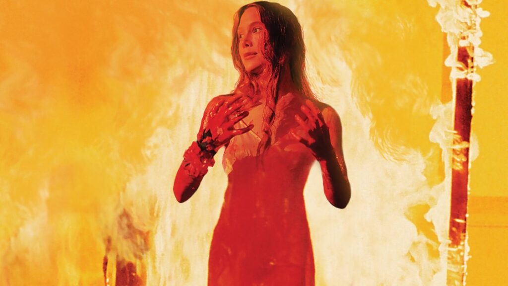 Sissy Spacek, empapada en sangre y con las manos alzadas, frente a un muro de llamas en la escena del baile de Carrie