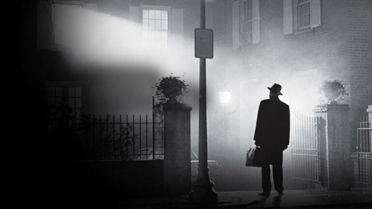 El padre Merrin bajo una farola frente a la casa iluminada entre la niebla, en El exorcista