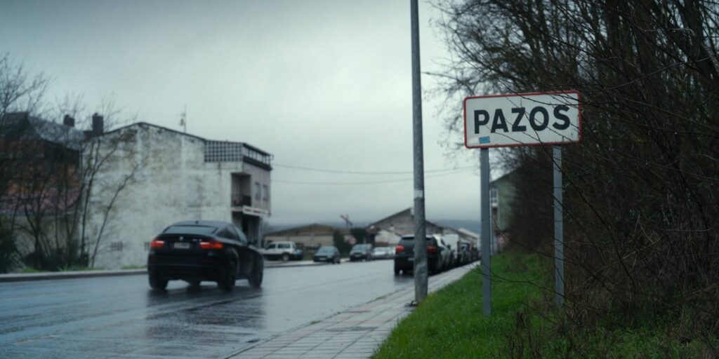 Cartel de entrada a Pazos junto a una carretera mojada, en un día gris, en el documental Desprotexida