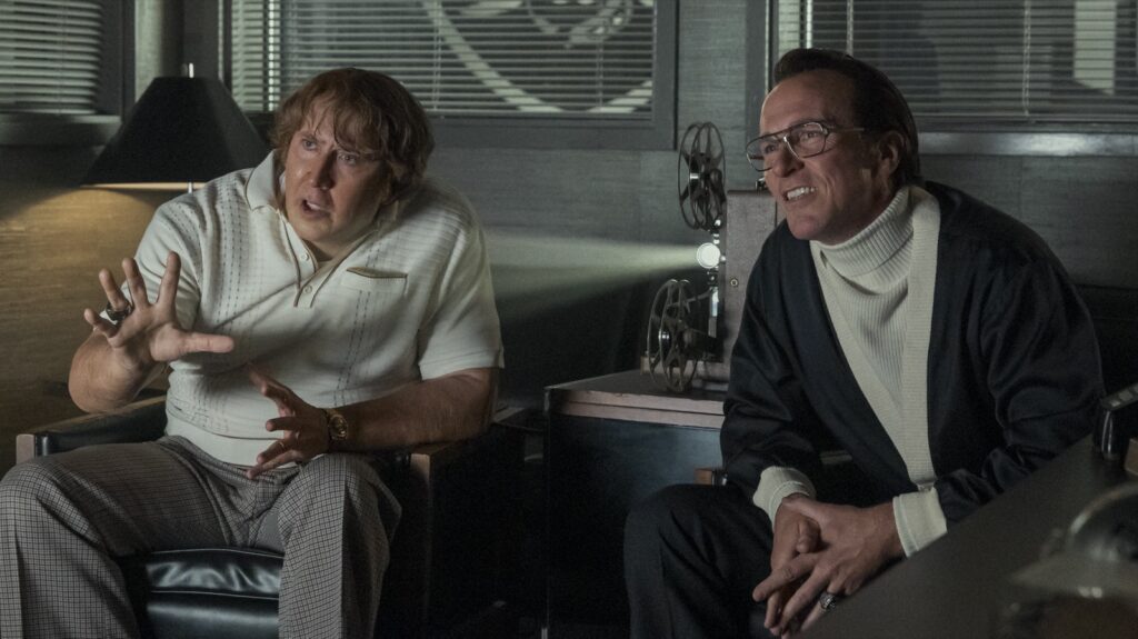 Nicolas Cage como John Madden y Christian Bale como Al Davis, sentados ante un proyector en un despacho, en Madden