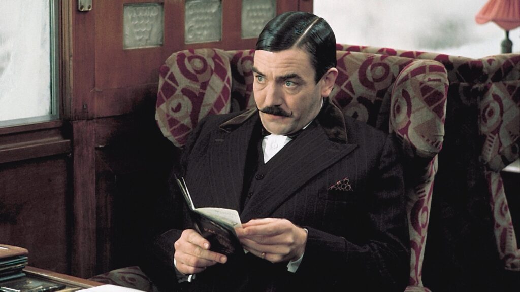 Albert Finney como Hércules Poirot, sentado en un compartimento del Orient Express con un documento en la mano, en Asesinato en el Orient Express (1974)