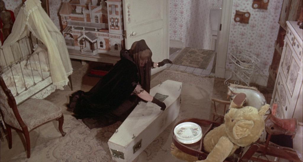 Shelley Winters vestida de negro se inclina sobre un pequeño ataúd en una habitación infantil.